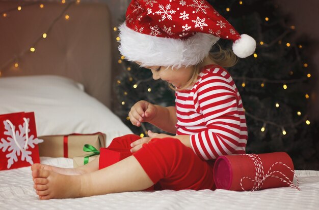 Little girl in Santa hat opening Christmas gift box Funny and expressive toddler enjoying gifts