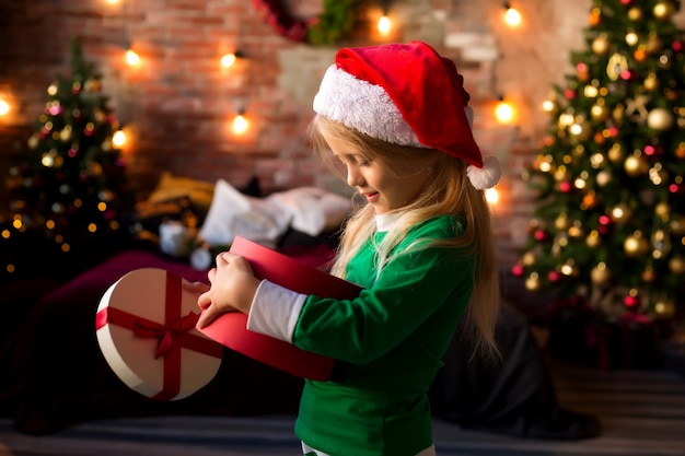 산타 모자에있는 어린 소녀는 선물 상자를 엽니 다