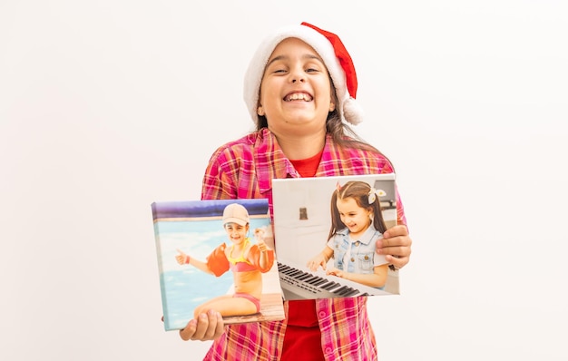 Little girl in Santa hat smiling and holding photo canvas in her hand. Christmas concept. Copy space.