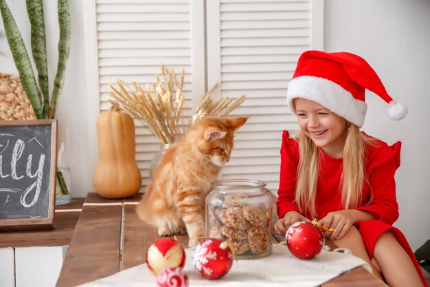 little girl in a Santa hat with a cat in the kitchen