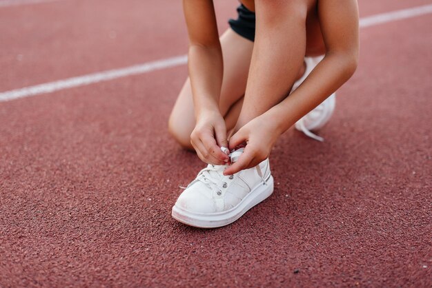 Una bambina si è seduta per allacciarsi i lacci delle scarpe prima di correre l'allenamento allo stadio durante il tramonto. sport per bambini e uno stile di vita sano.