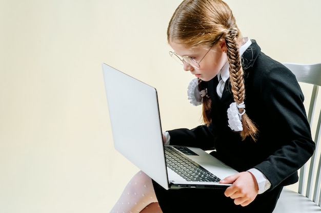 La bambina dell'età scolare guarda in un computer portatile su un fondo leggero, dipendenza da internet