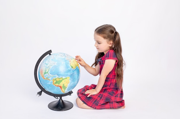 little girl school girl 7 years old sitting in a red dress with a globe on white