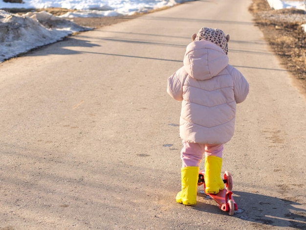 Little girl on a scooter in rubber boots in spring