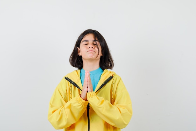 Little girl showing clasped hands in pleading gesture in shirt, jacket and looking hopeful , front view.