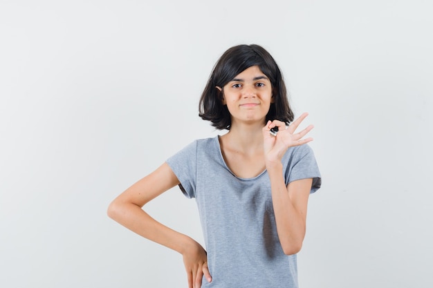 Little girl showing ok gesture in t-shirt and looking confident. front view.