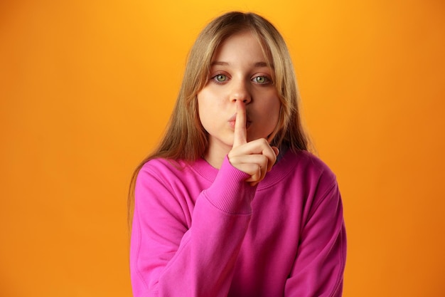 Little girl showing silence gesture against yellow background
