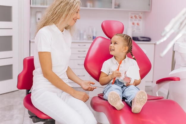 A little girl shows how she brushes the teeth for the woman dentist in a dental clinic