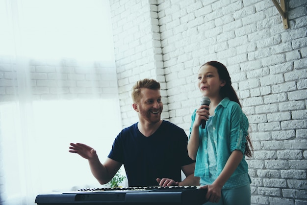 Photo little girl sings while dad plays synthesizer.