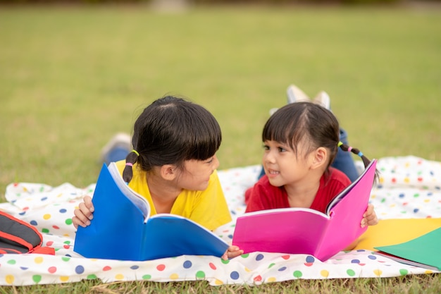 公園で一緒に本を読んでいる少女と妹。一緒に屋外で勉強を楽しんでいる愛らしいアジアの子供たち。教育、インテリジェンスの概念