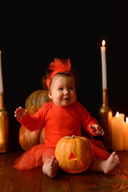 Little girl sits on a background of Jack pumpkins and candles on a black background.