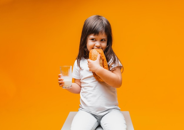 小さな女の子は黄色の背景の上の立方体に座って、パンの健康食品天然物パンを食べます