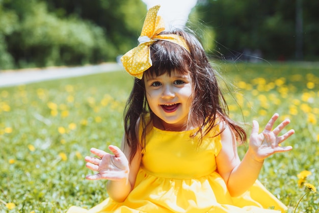 小さな女の子は黄色のタンポポと草の上に座っています子供は春の花の中で新鮮な緑の草に座っています