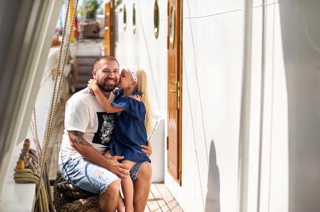 Photo a little girl sits in her father's arms and kisses him on the cheek on the deck of a large lithuania