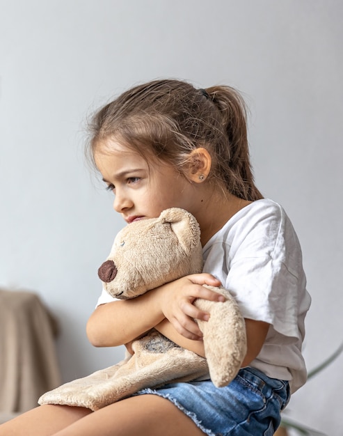 A little girl sits and holds a teddy bear tightly in her hands.