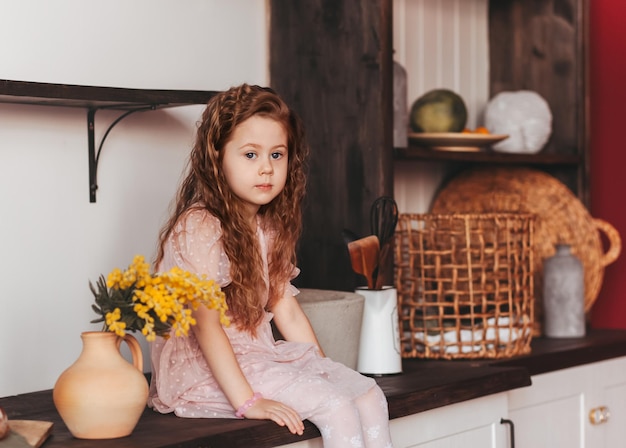 A little girl sits on the kitchen table in the kitchen. Household help