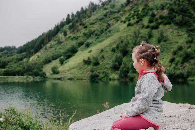 Маленькая девочка сидит и смотрит на озеро