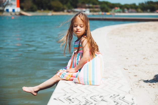 小さな女の子は、夏休みの屋外で市の湖の近くの桟橋に座っています