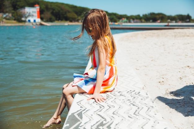 A little girl sits on a pier near the city lake outdoors summer vacation