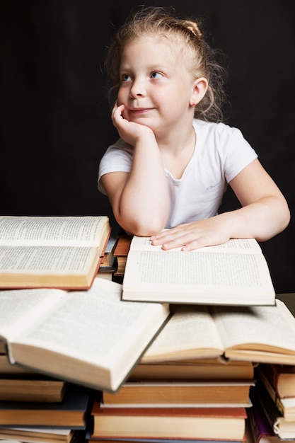 little girl sits on a pile of books and dreams. Education and training.