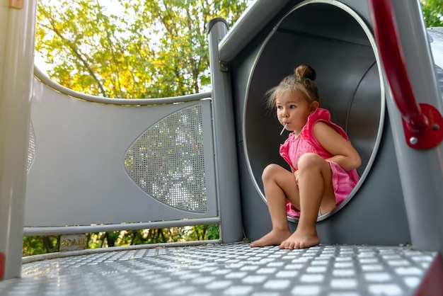 a little girl sits on a platform in a metal pipe