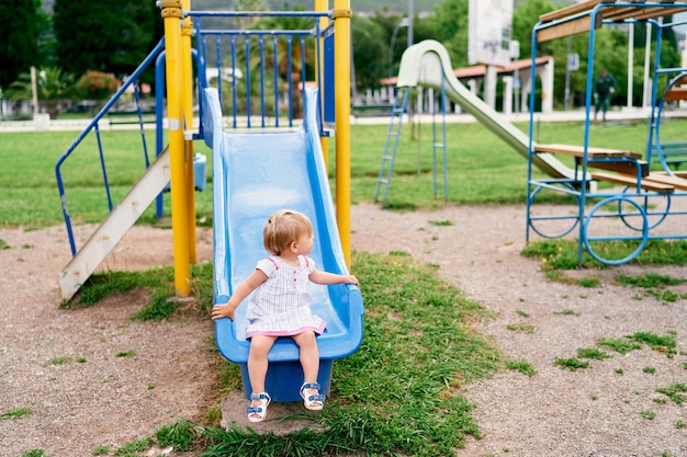 Little girl sits on a slide in the playground turning her head