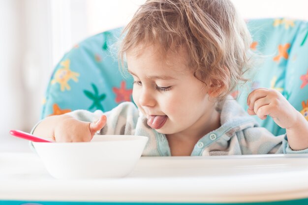 小さな女の子がテーブルに座ってスプーンで食べる