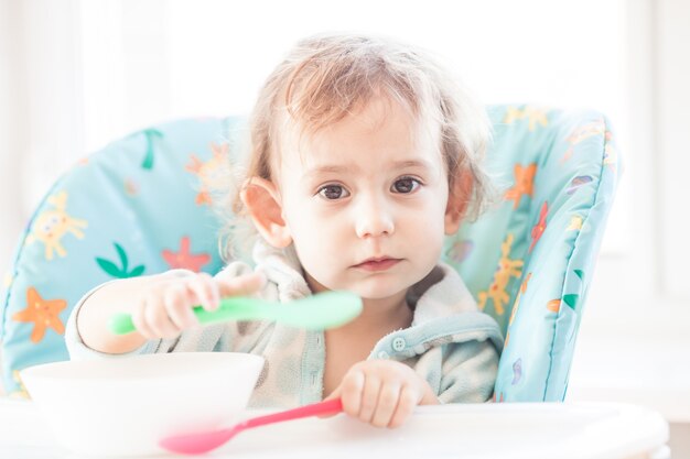 Little girl sits at a table and eating with two spoons. The concept of super efficiency