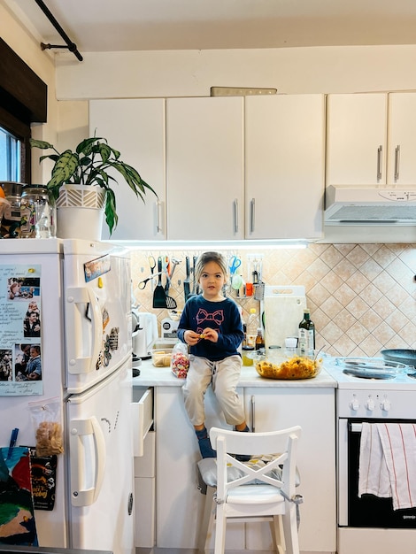 Photo little girl sits on the table in the kitchen near the refrigerator