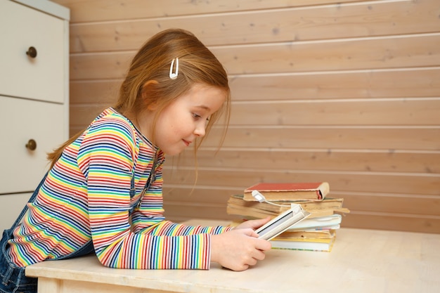 little girl sits at a table and reads an e-book.