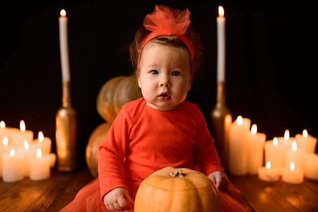 Little girl sits with Jack pumpkins and candles on a black wall. Close-up.