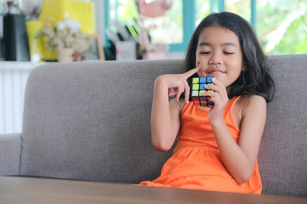 Photo little girl sitting alone in the sofa playing rubik's cubes