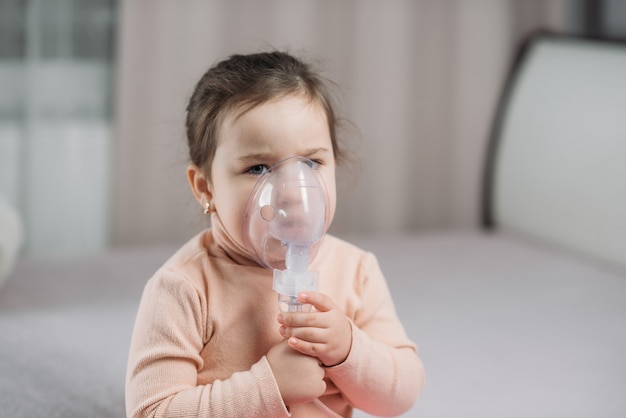 Little girl sitting on the bed in the bedroom with oxygen mask