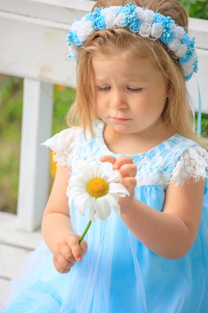 Little girl sitting on a bench in a blue dress with a chamomile