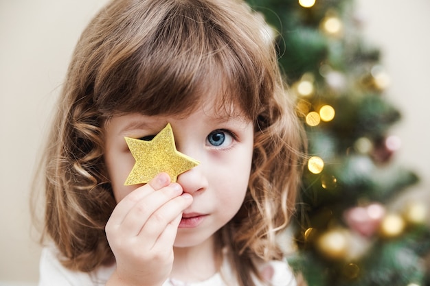 飾られたクリスマスツリーの横に座っている少女