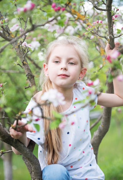 사과 정원에서 꽃이 만발한 나무에 앉아 어린 소녀