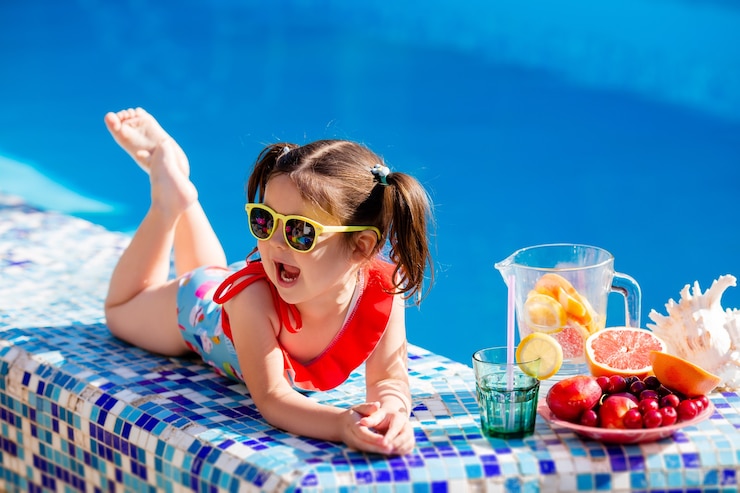 Photo little girl sitting by the pool drinking lemonade