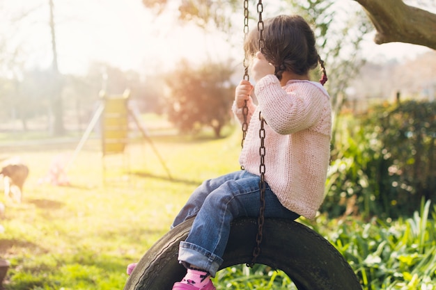 Photo little girl sitting on the car tire swing in the park