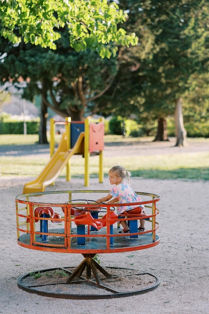 Foto piccola ragazza seduta su un carosello che tiene il volante nel parco giochi