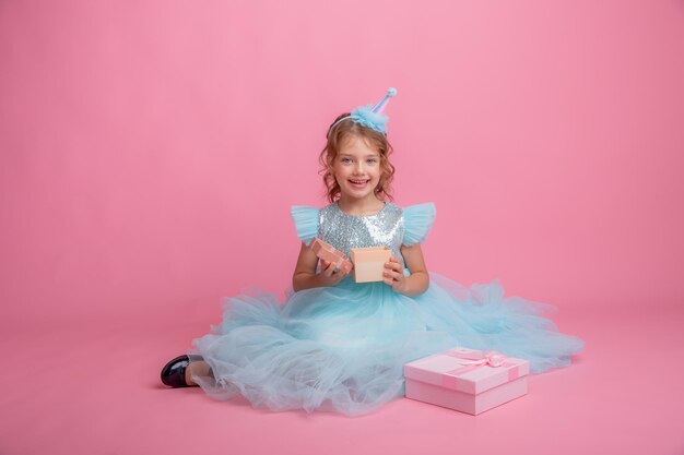 little girl sitting celebrating birthday on pink background, beautiful princess dress