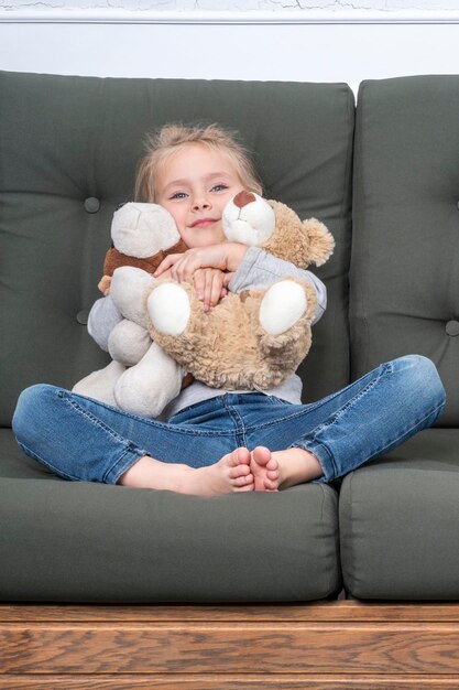 Little girl sitting on the couch, two hands hugging soft toys