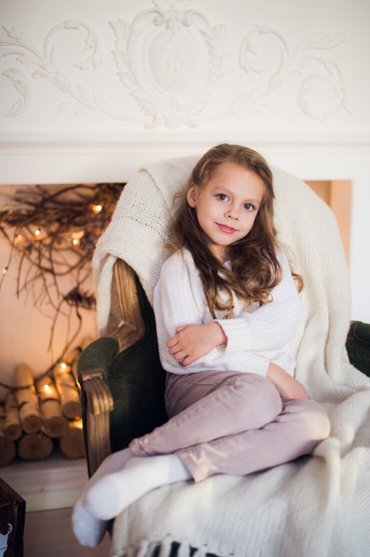 Little girl sitting on cozy armchair wrapped in a blanket