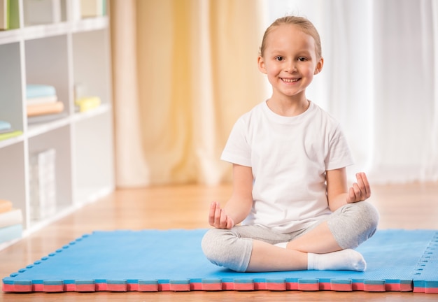 Little girl sitting on exercise mat.