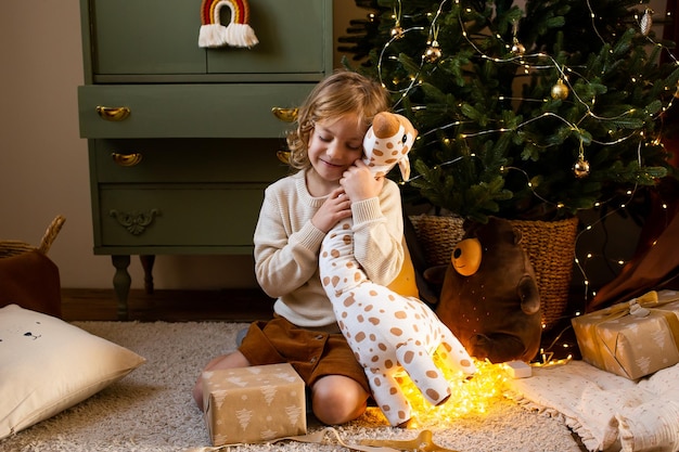 Little girl sitting on floor in Christmas home and hugging her cute toy giraffe
