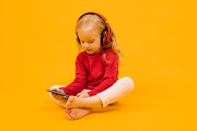 little girl sitting on the floor in headphones and sitting on the phone on a yellow wall