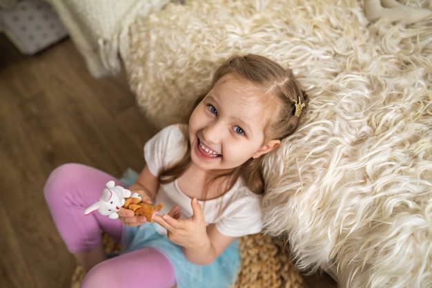 La bambina che si siede sul pavimento che si appoggia sul sofà e che gioca giocando con il dito gioca