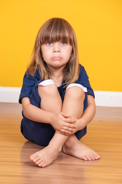 Bambina seduta sul pavimento con una benda sul ginocchio che simula un livido