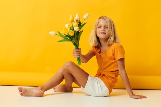 Маленькая девочка сидит на полу с букетом желтых цветов весело желтый фон