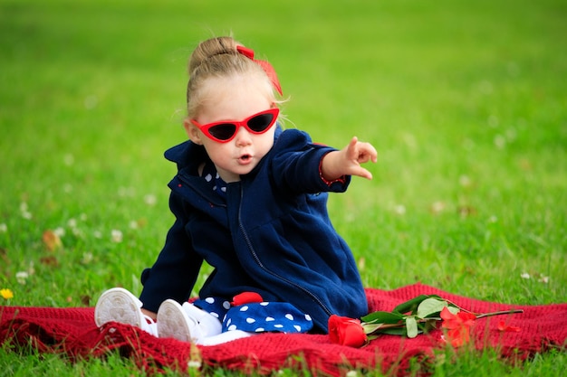 Bambina seduta sull'erba nel parco indossando occhiali da sole