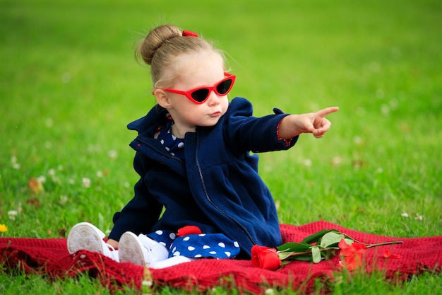 Little girl sitting on the grass in the park wearing sunglasses